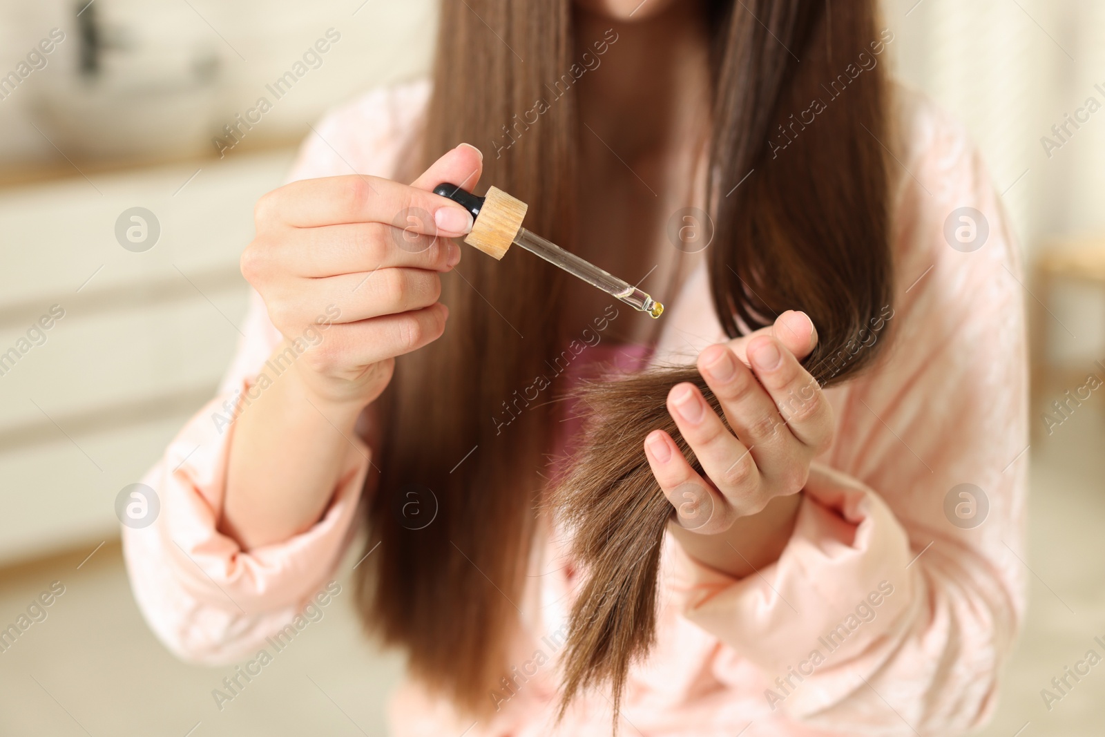 Teenage girl applying serum onto her hair at home, closeup Photo of Teenage girl applying serum onto her hair at home, closeup