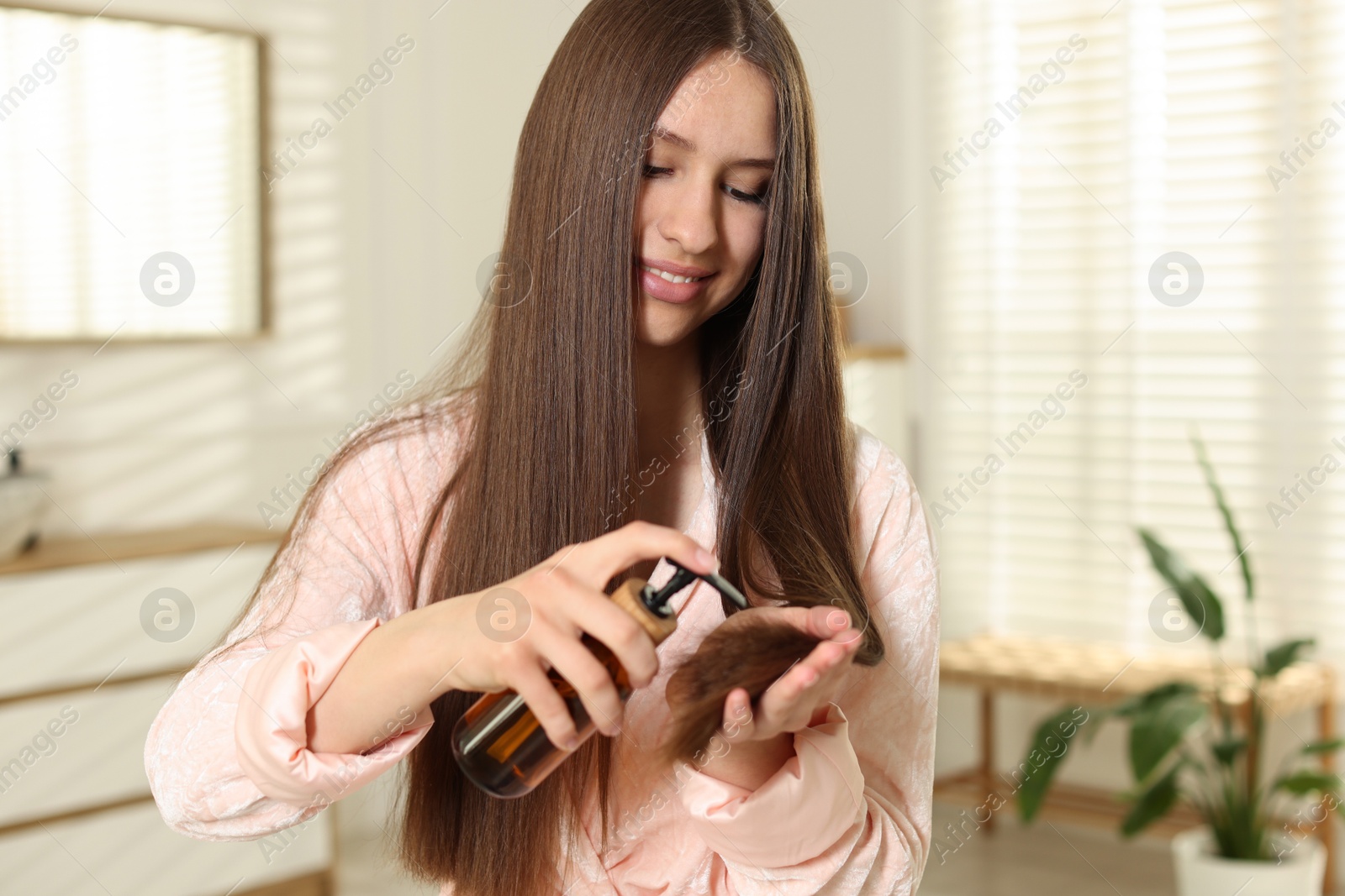 Smiling teenage girl applying cosmetic product onto her hair at home Photo of Smiling teenage girl applying cosmetic product onto her hair at home