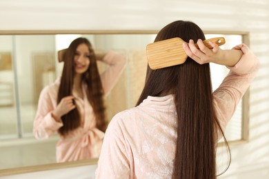 Photo of Smiling teenage girl brushing her shiny hair near mirror at home, selective focus