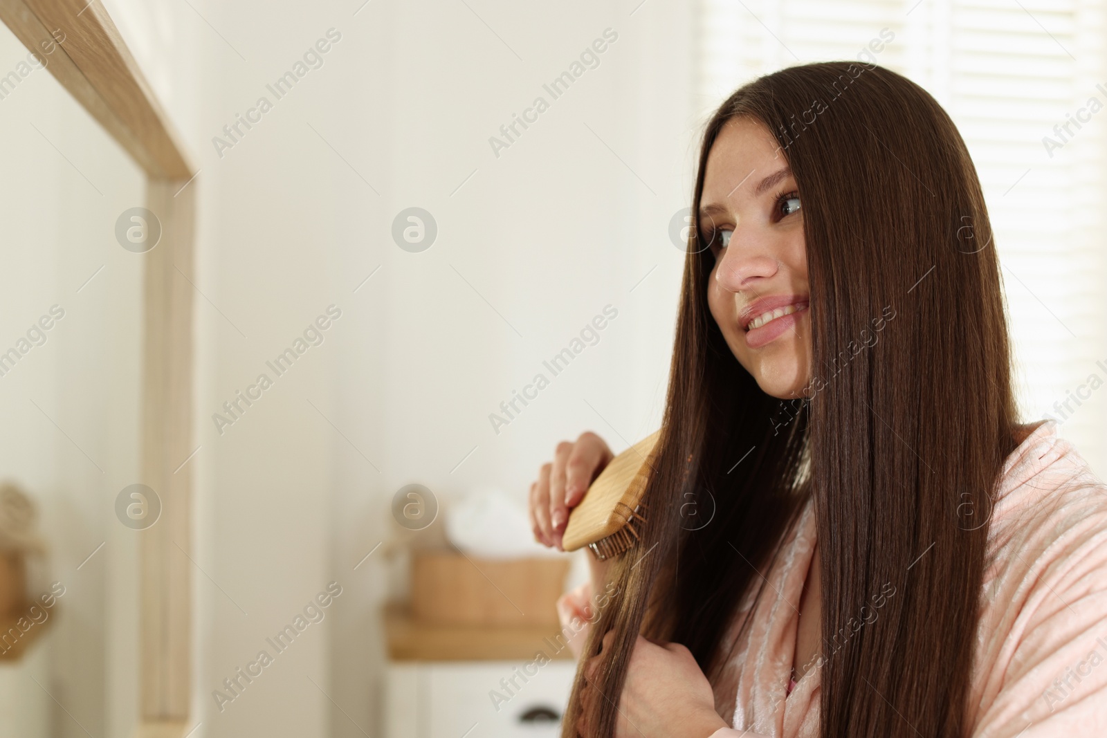 Smiling teenage girl brushing her shiny hair near mirror at home Photo of Smiling teenage girl brushing her shiny hair near mirror at home