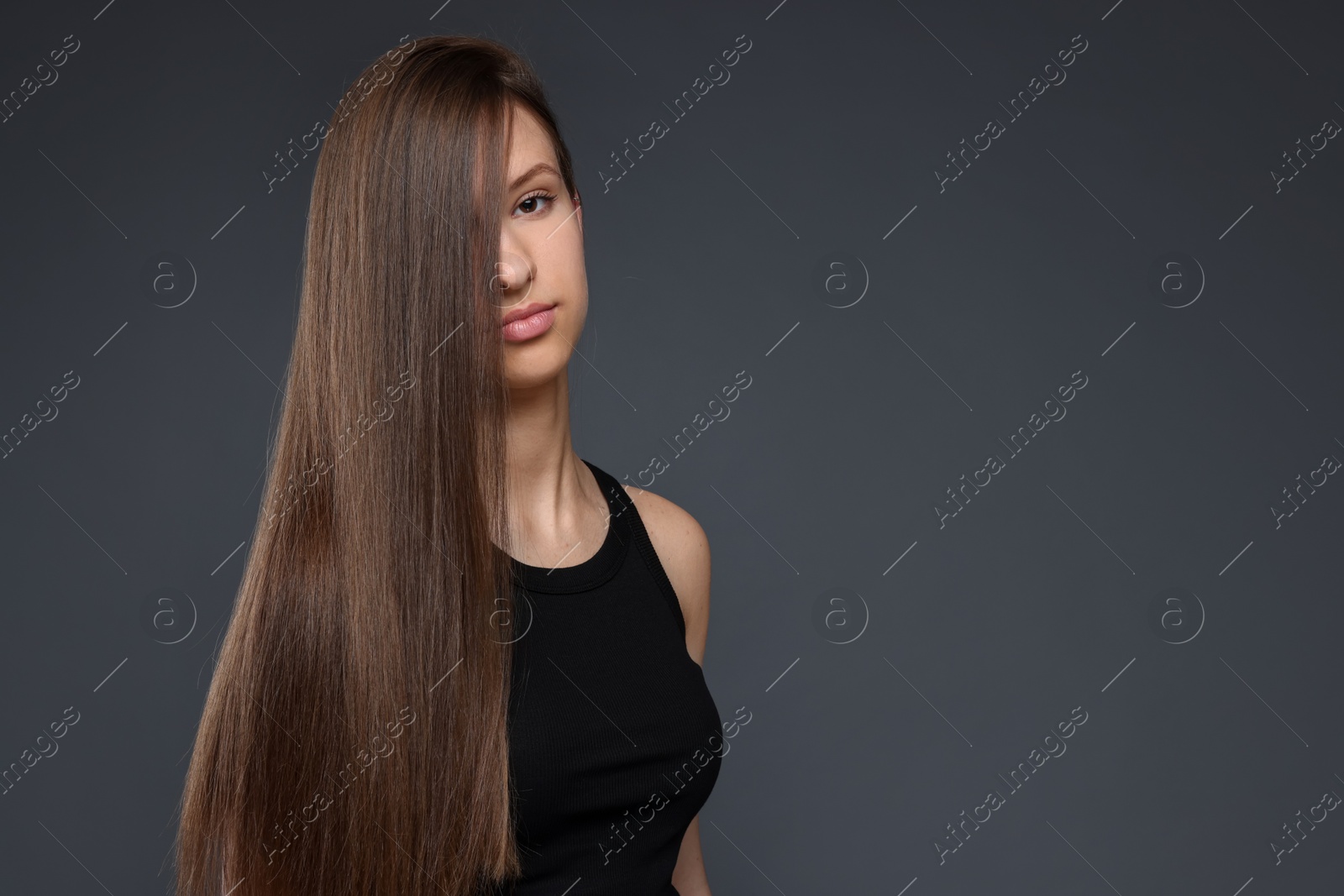 Teenage girl with healthy long hair on dark grey background. Space for text Photo of Teenage girl with healthy long hair on dark grey background. Space for text