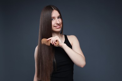 Photo of Smiling teenage girl brushing her healthy long hair on dark grey background