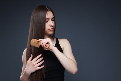 Photo of Beautiful teenage girl brushing her healthy long hair on dark grey background. Space for text
