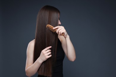 Photo of Teenage girl brushing her healthy long hair on dark grey background