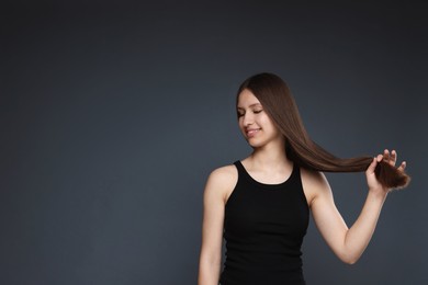 Photo of Smiling teenage girl with healthy long hair on dark grey background. Space for text