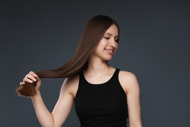 Photo of Smiling teenage girl with healthy long hair on dark grey background