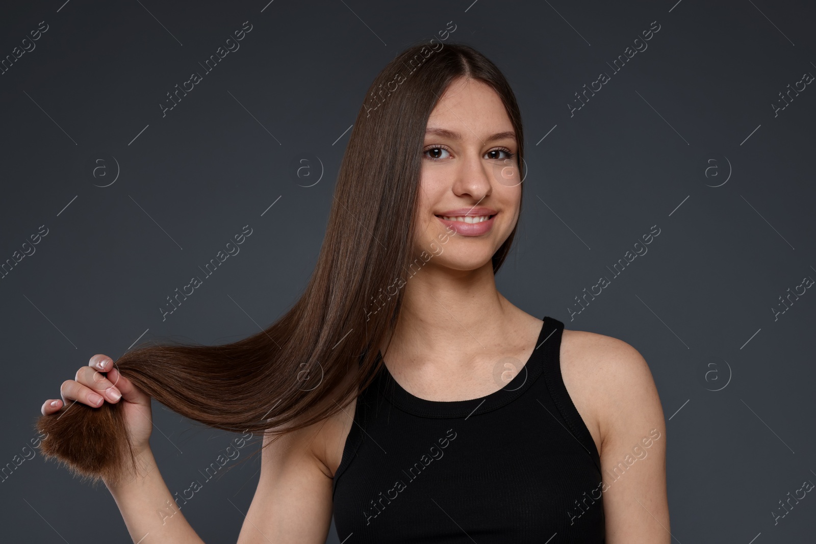Portrait of smiling teenage girl with healthy long hair on dark grey background Photo of Portrait of smiling teenage girl with healthy long hair on dark grey background