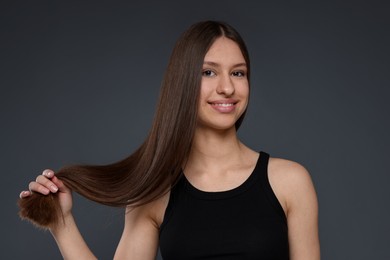Photo of Portrait of smiling teenage girl with healthy long hair on dark grey background