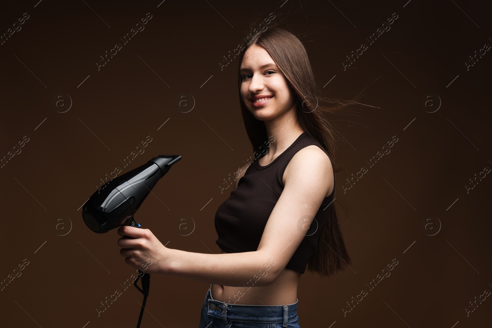 Smiling teenage girl with hair dryer on brown background Photo of Smiling teenage girl with hair dryer on brown background