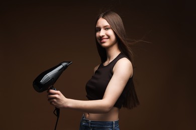Photo of Smiling teenage girl with hair dryer on brown background