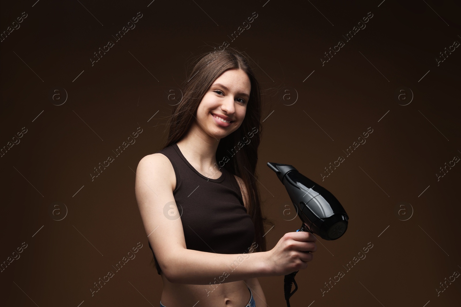 Smiling teenage girl with hair dryer on brown background Photo of Smiling teenage girl with hair dryer on brown background