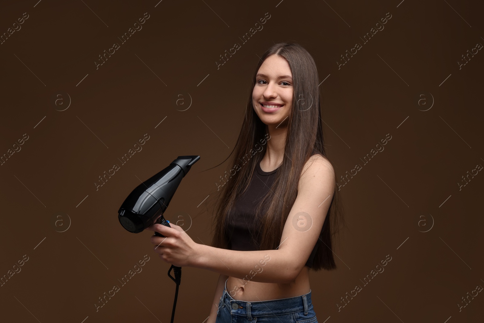 Smiling teenage girl with hair dryer on brown background Photo of Smiling teenage girl with hair dryer on brown background