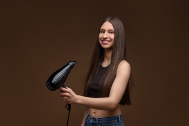 Photo of Smiling teenage girl with hair dryer on brown background