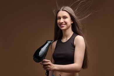 Photo of Smiling teenage girl with hair dryer on brown background