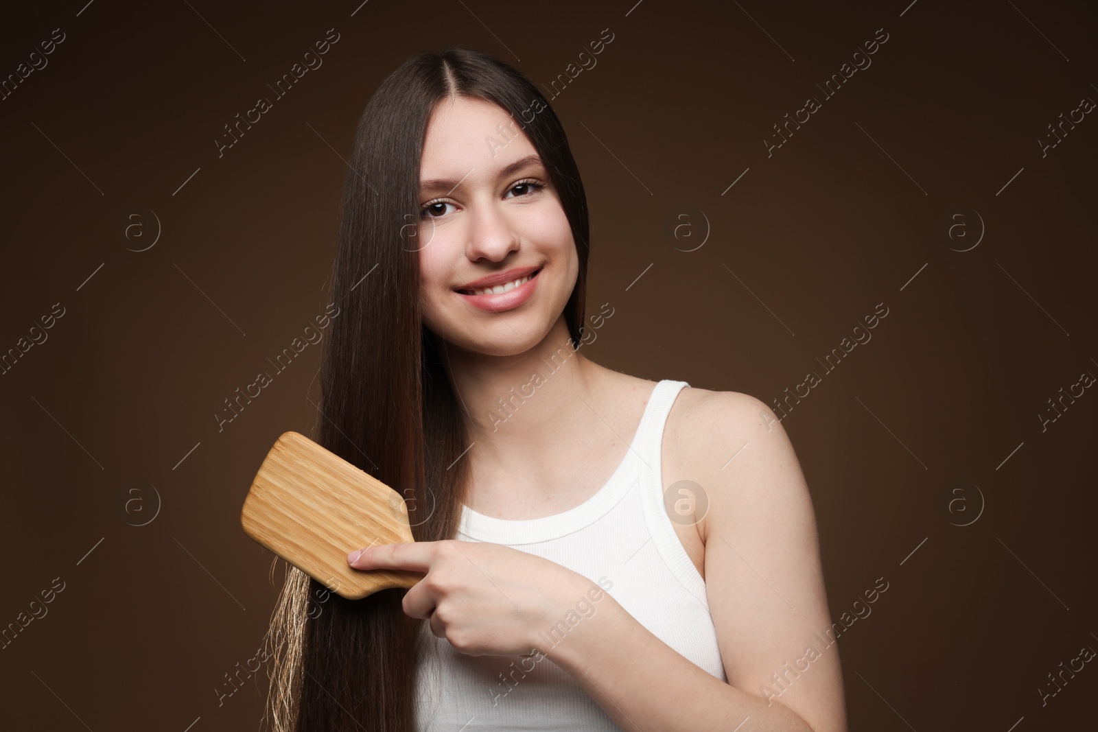 Smiling teenage girl brushing her healthy long hair on brown background Photo of Smiling teenage girl brushing her healthy long hair on brown background