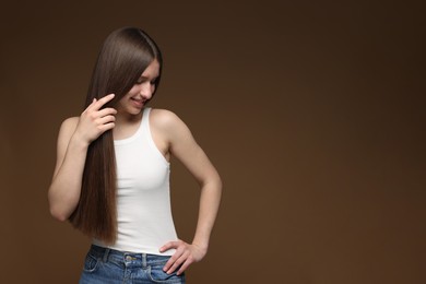 Photo of Smiling teenage girl with healthy long hair on brown background. Space for text