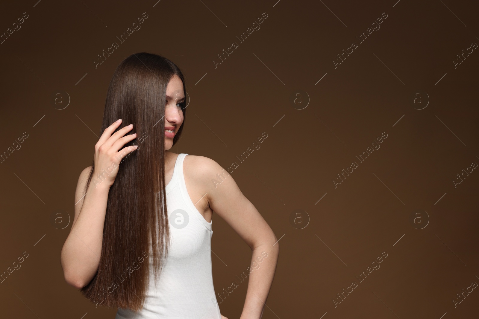 Smiling teenage girl with healthy long hair on brown background. Space for text Photo of Smiling teenage girl with healthy long hair on brown background. Space for text