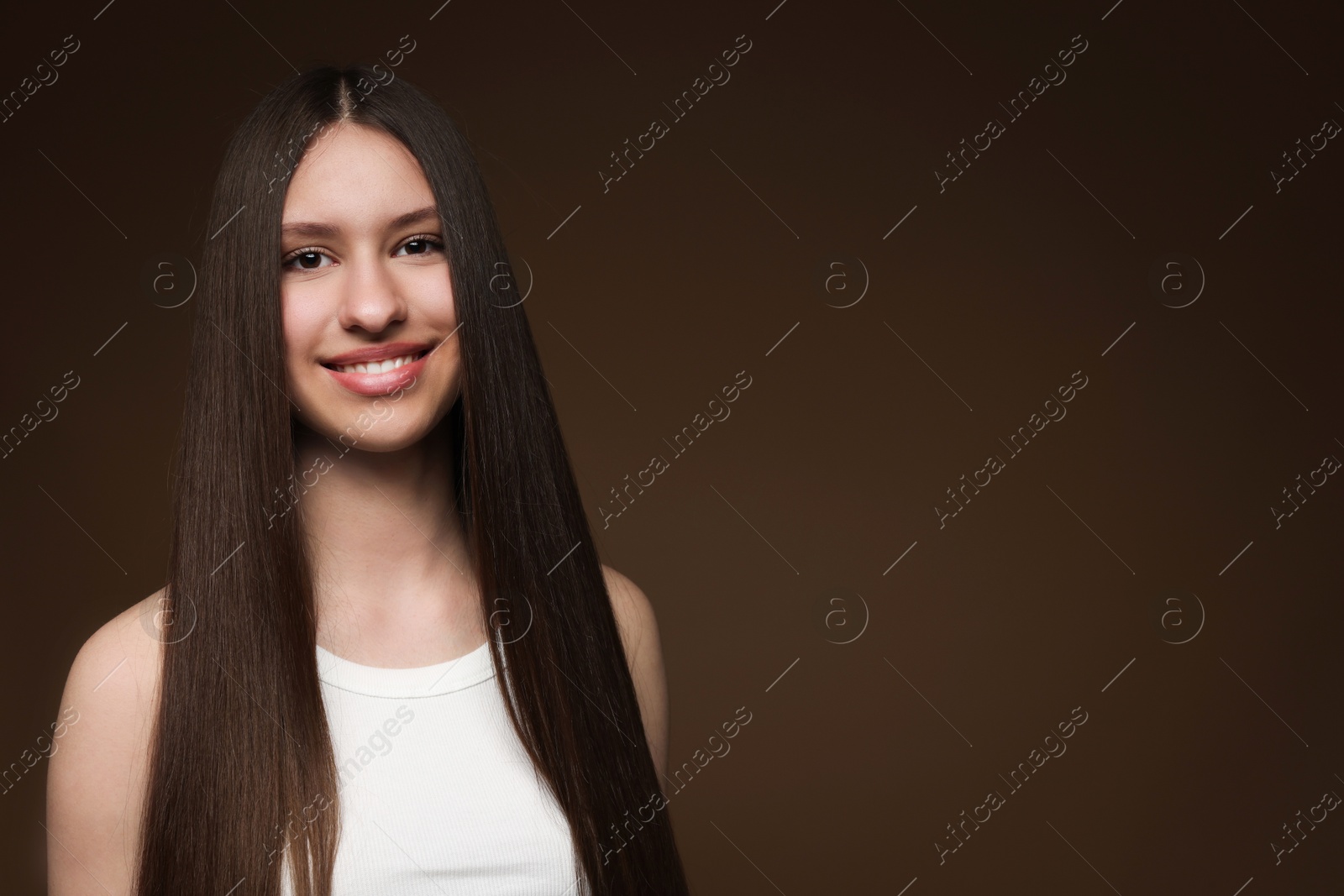 Portrait of smiling teenage girl with healthy long hair on brown background. Space for text Photo of Portrait of smiling teenage girl with healthy long hair on brown background. Space for text