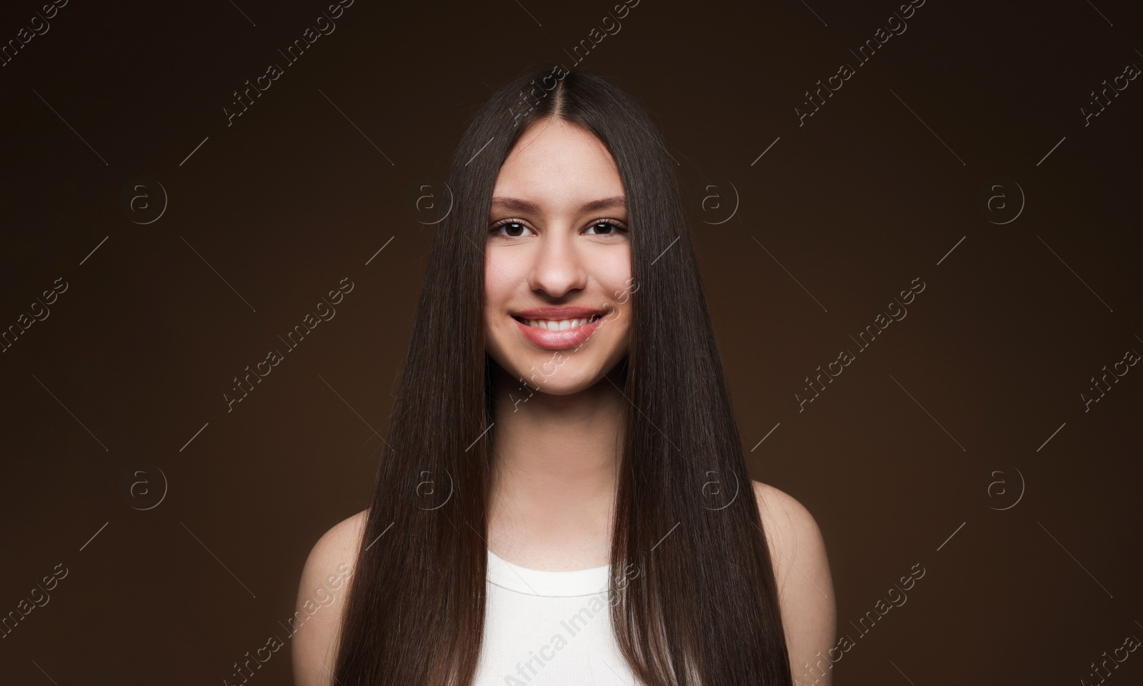 Portrait of smiling teenage girl with healthy long hair on brown background Photo of Portrait of smiling teenage girl with healthy long hair on brown background