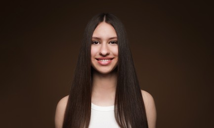 Photo of Portrait of smiling teenage girl with healthy long hair on brown background