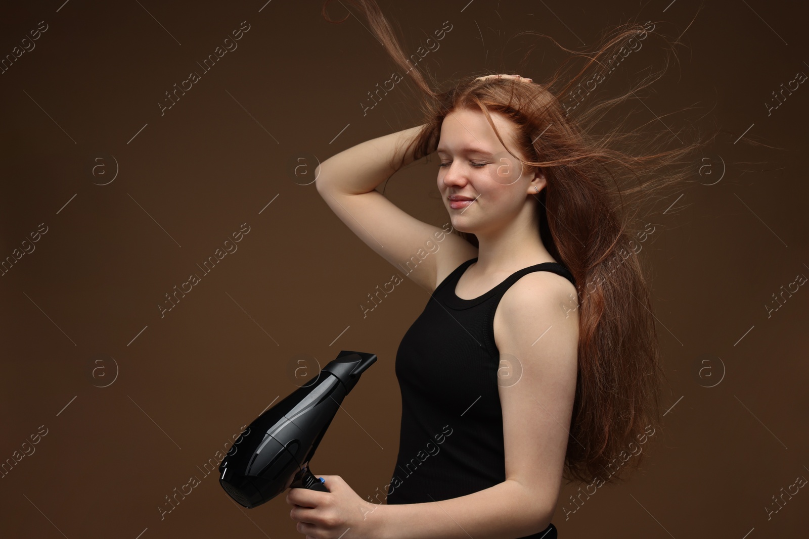Beautiful teenage girl with hair dryer on brown background Photo of Beautiful teenage girl with hair dryer on brown background