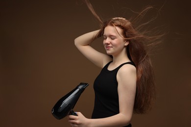 Photo of Beautiful teenage girl with hair dryer on brown background