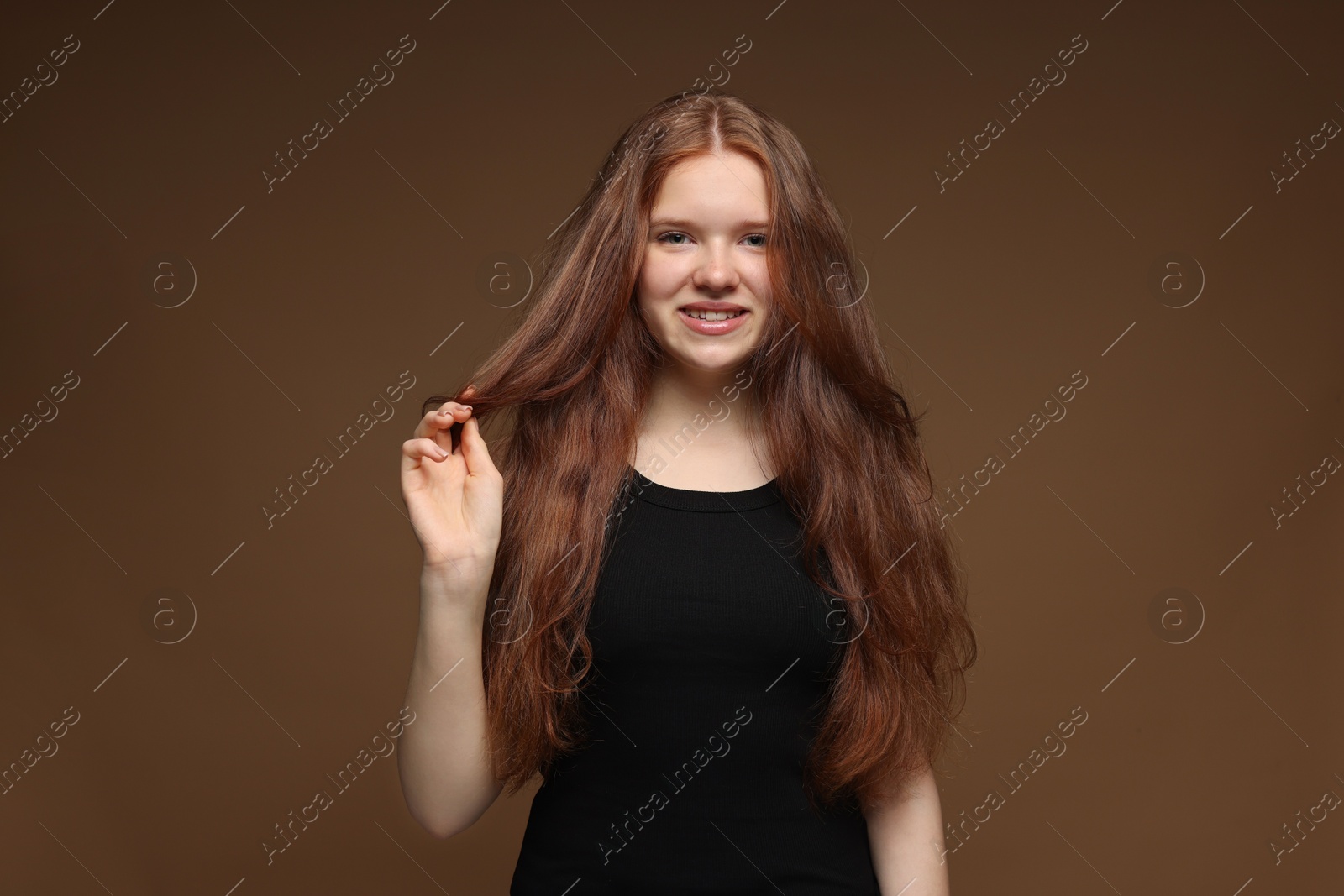 Portrait of smiling teenage girl with healthy wavy hair on brown background Photo of Portrait of smiling teenage girl with healthy wavy hair on brown background