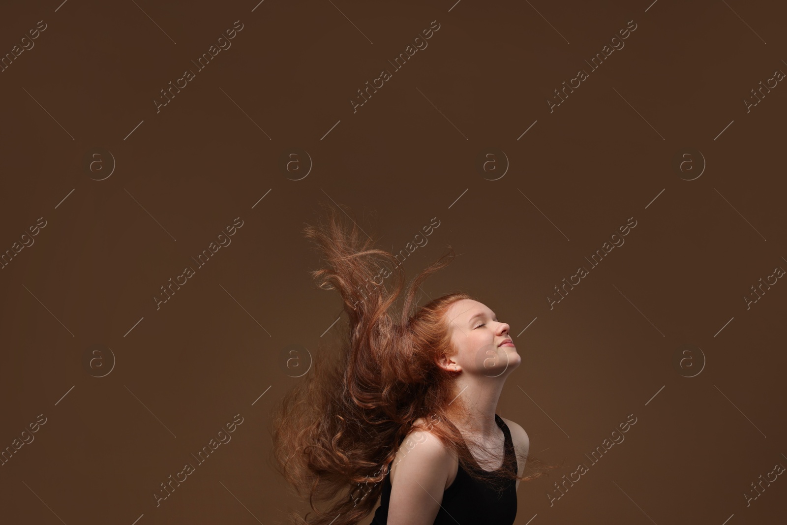 Teenage girl with healthy wavy hair on brown background Photo of Teenage girl with healthy wavy hair on brown background