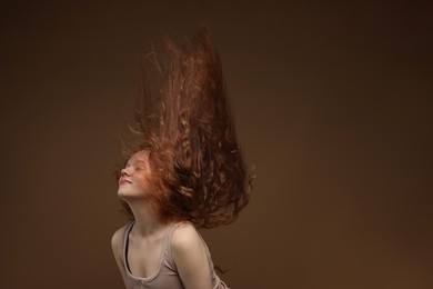 Photo of Teenage girl with healthy wavy hair on brown background