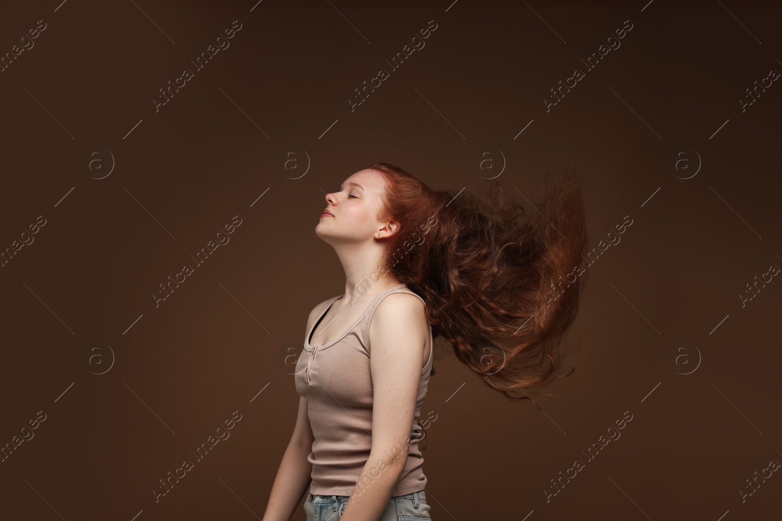 Teenage girl with healthy wavy hair on brown background Photo of Teenage girl with healthy wavy hair on brown background