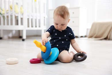 Photo of Cute little baby playing with toy pyramid in room