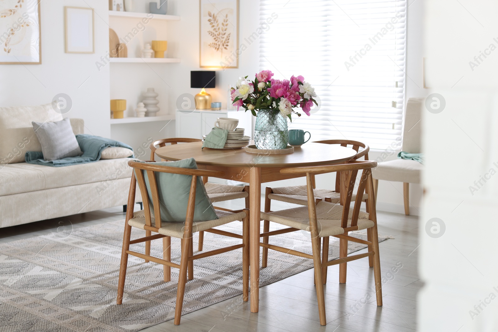 Dining table with beautiful flowers and dishware in room. Interior design Photo of Dining table with beautiful flowers and dishware in room. Interior design