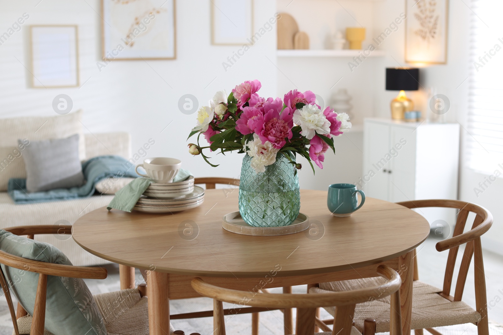 Dining table with beautiful flowers and dishware in room. Interior design Photo of Dining table with beautiful flowers and dishware in room. Interior design