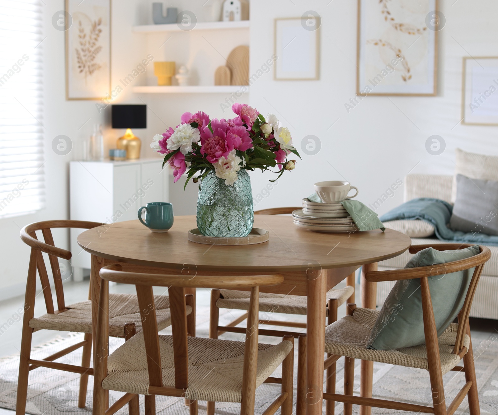 Dining table with beautiful flowers and dishware in room. Interior design Photo of Dining table with beautiful flowers and dishware in room. Interior design