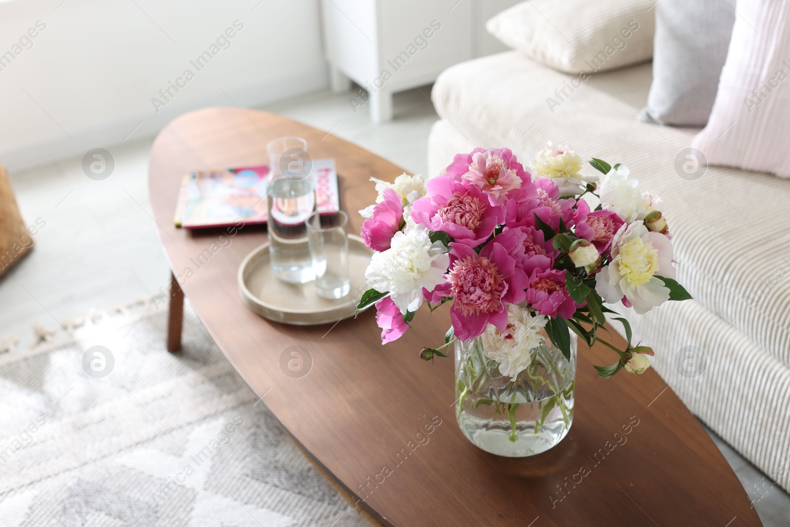 Bouquet of beautiful peonies and water on coffee table indoors. Interior design Photo of Bouquet of beautiful peonies and water on coffee table indoors. Interior design