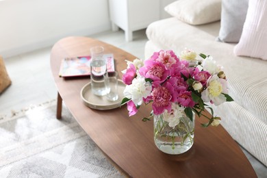 Photo of Bouquet of beautiful peonies and water on coffee table indoors. Interior design