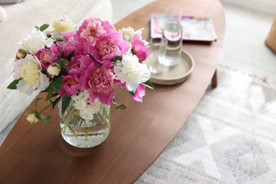 Photo of Bouquet of beautiful peonies and water on coffee table indoors. Interior design