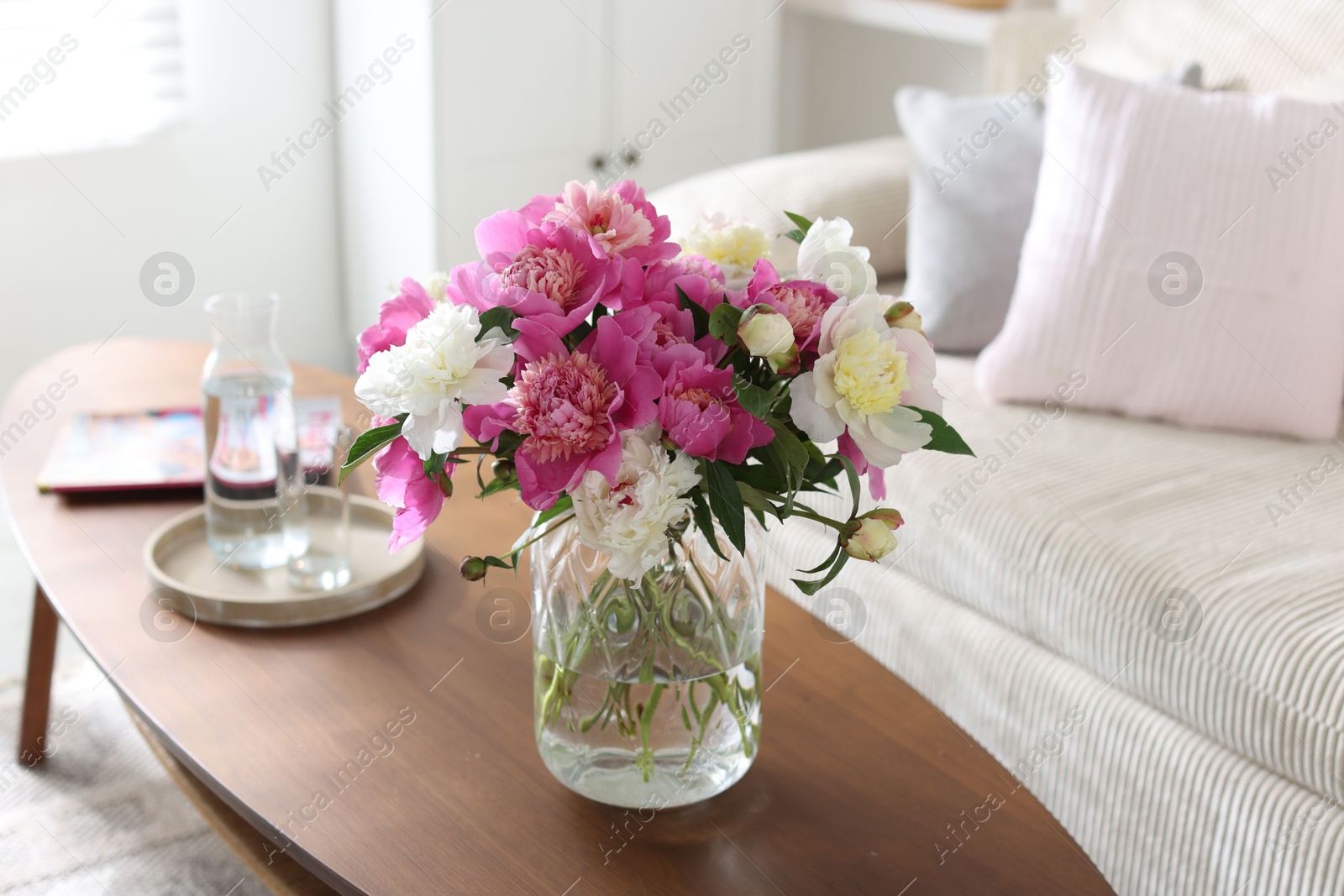 Bouquet of beautiful peonies and water on coffee table indoors. Interior design Photo of Bouquet of beautiful peonies and water on coffee table indoors. Interior design
