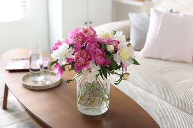 Photo of Bouquet of beautiful peonies and water on coffee table indoors. Interior design