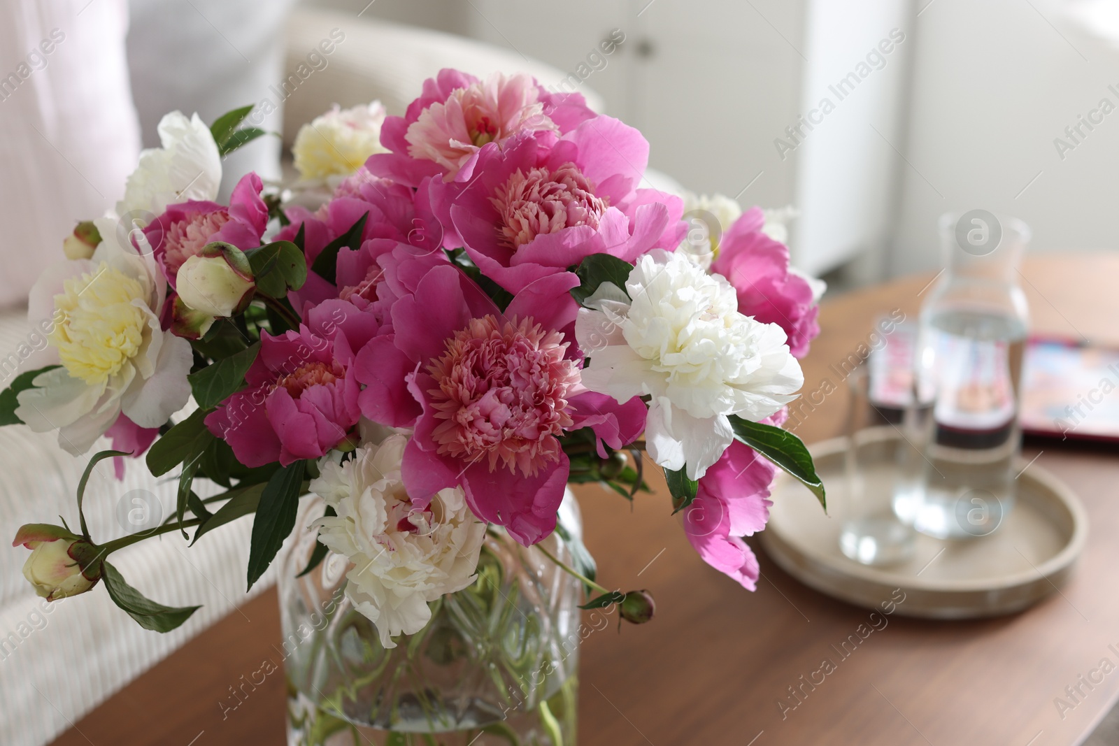 Bouquet of beautiful peonies and water on coffee table indoors, closeup. Interior design Photo of Bouquet of beautiful peonies and water on coffee table indoors, closeup. Interior design