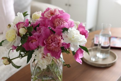 Photo of Bouquet of beautiful peonies and water on coffee table indoors, closeup. Interior design