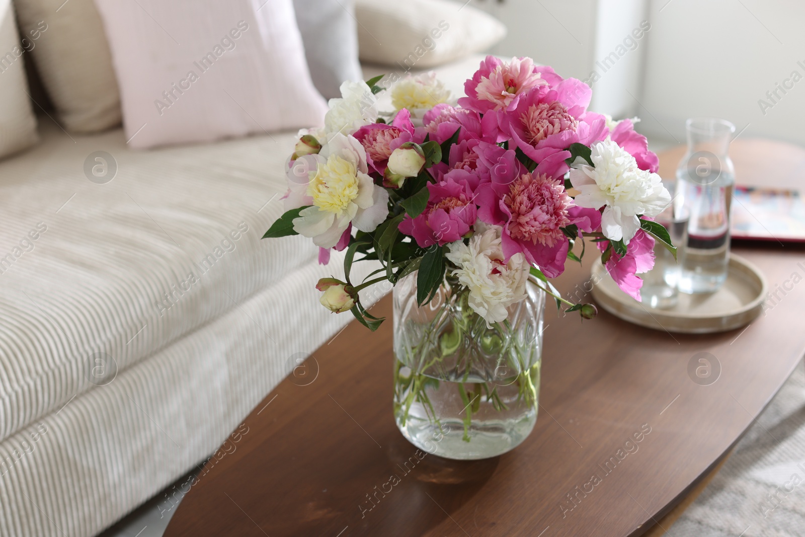 Bouquet of beautiful peonies and water on coffee table indoors, closeup with space for text. Interior design Photo of Bouquet of beautiful peonies and water on coffee table indoors, closeup with space for text. Interior design
