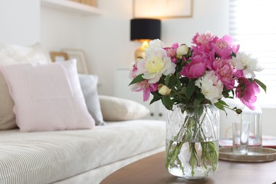 Photo of Bouquet of beautiful peonies and water on coffee table indoors, closeup with space for text. Interior design