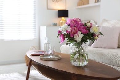 Photo of Bouquet of beautiful peonies and water on coffee table indoors, space for text. Interior design