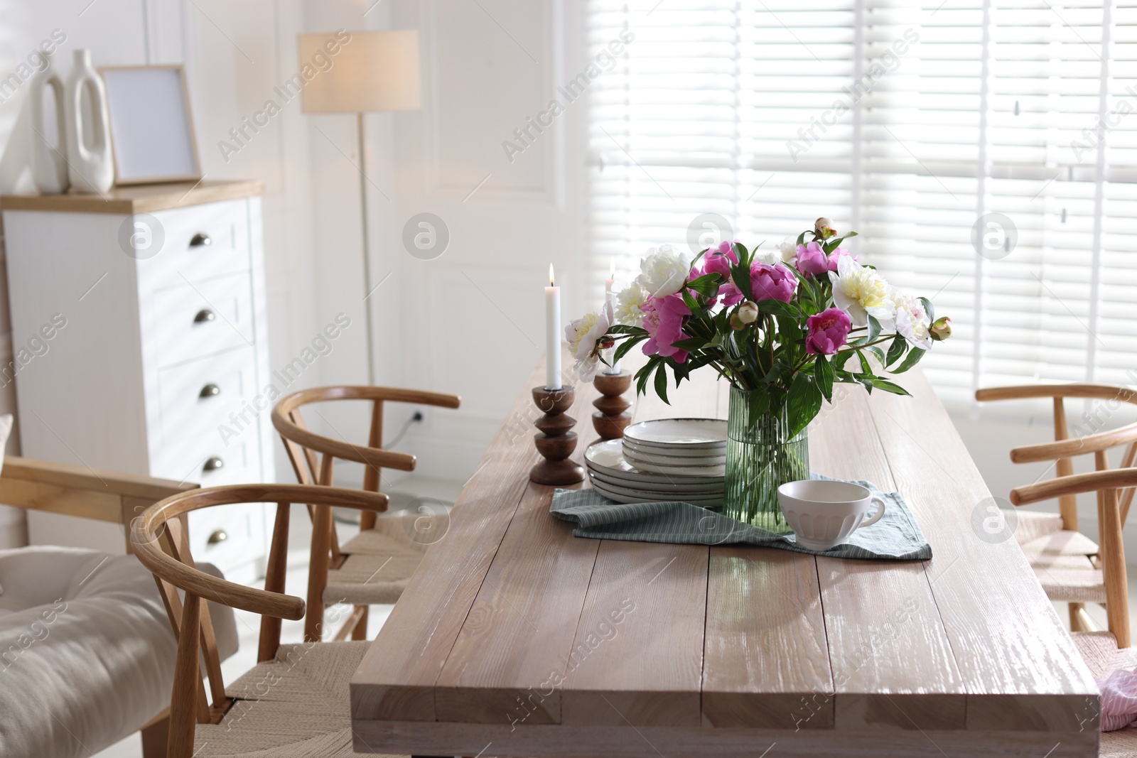 Dining table with beautiful flowers and dishware in room. Interior design Photo of Dining table with beautiful flowers and dishware in room. Interior design