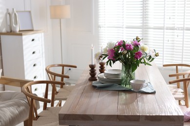 Photo of Dining table with beautiful flowers and dishware in room. Interior design