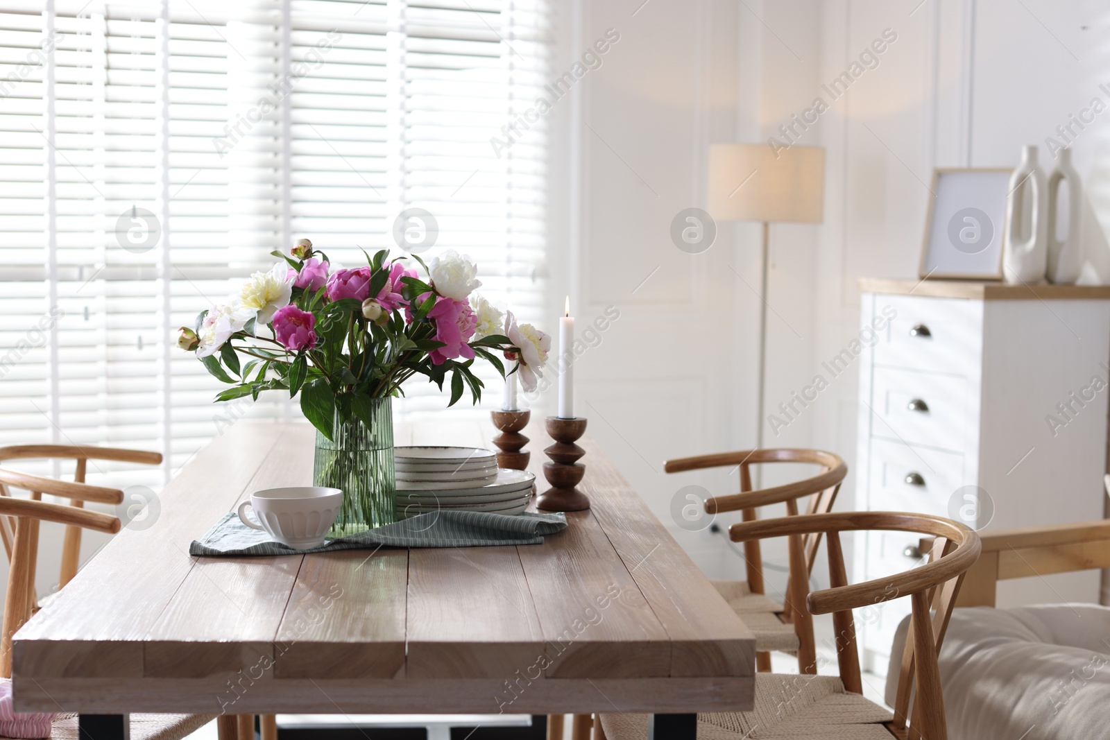 Dining table with beautiful flowers and dishware in room. Interior design Photo of Dining table with beautiful flowers and dishware in room. Interior design