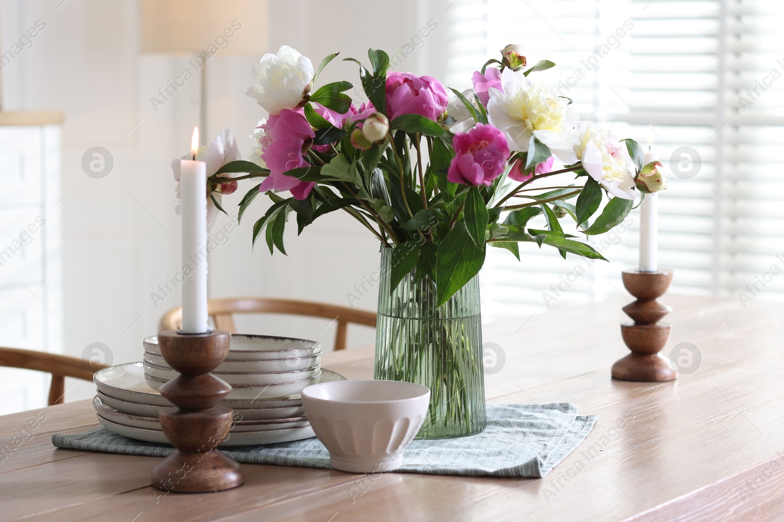 Dining table with beautiful flowers and dishware in room. Interior design Photo of Dining table with beautiful flowers and dishware in room. Interior design