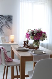 Photo of Beautiful table setting with bouquet of peonies in dining room. Interior design