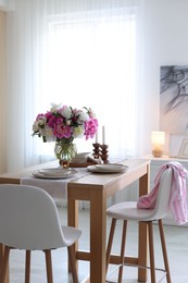 Photo of Beautiful table setting with bouquet of peonies in dining room. Interior design